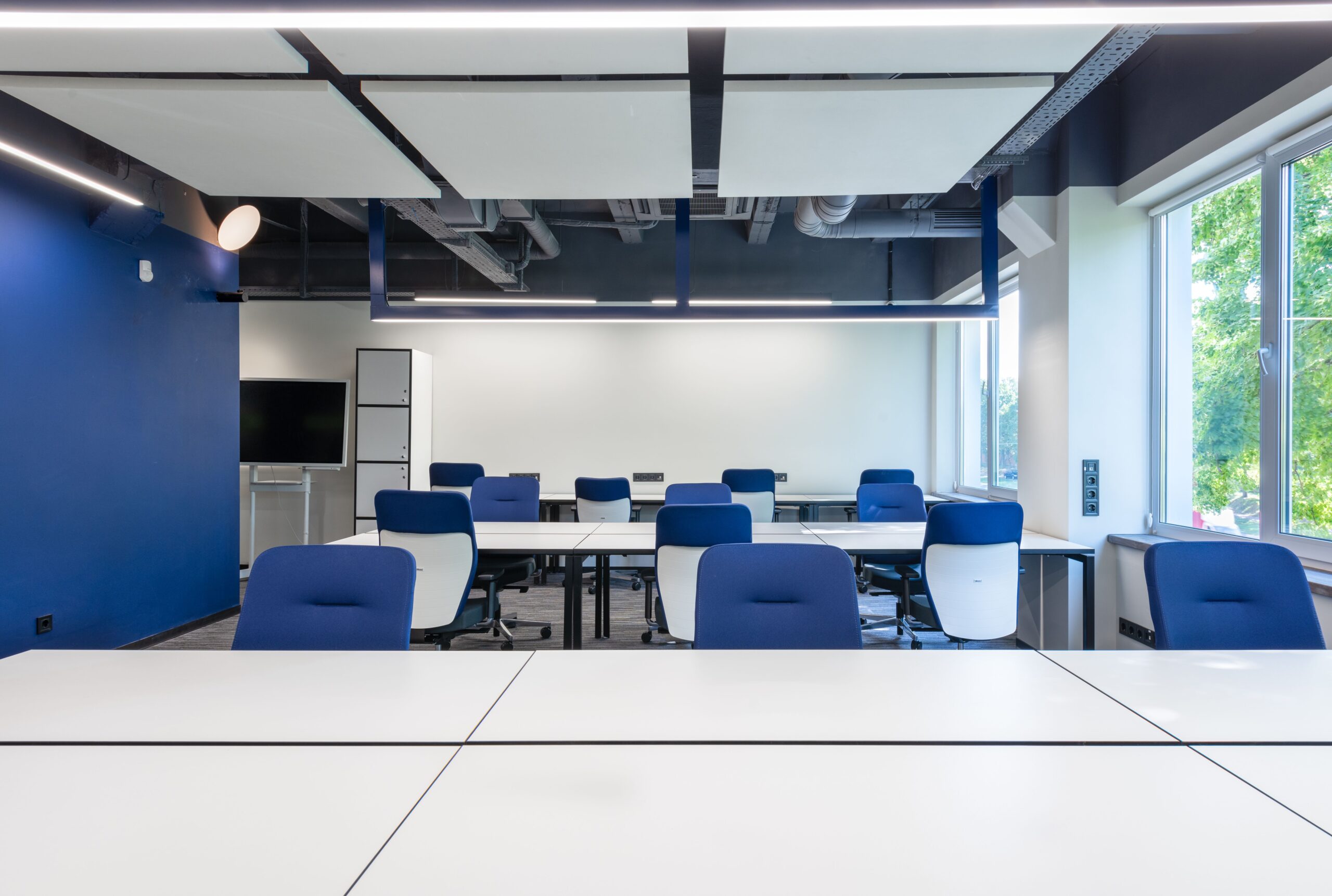 Spacious modern business workspace with organized white desks, blue chairs and daylight.